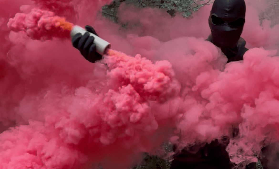 Masked football supporter surrounded by coloured smoke